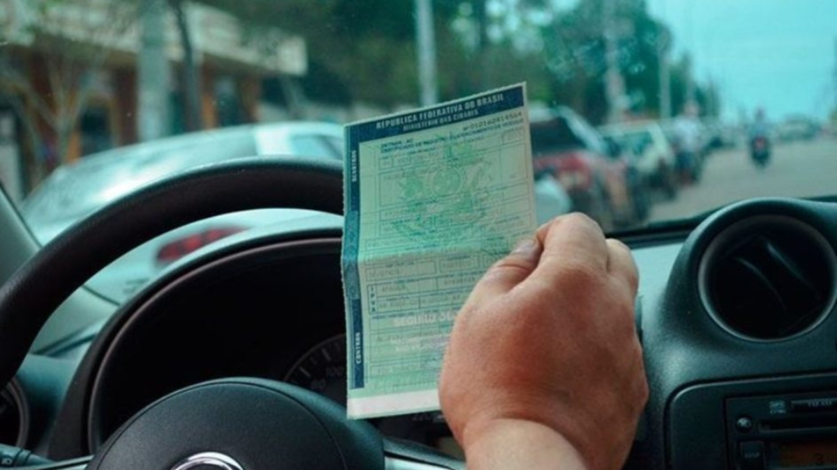 Pessoa segurando o documento de licenciamento veicular na mão