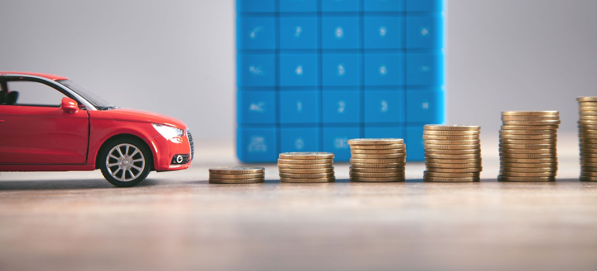 Imagem ilustrativa de um carro vermelho e algumas moedas empilhadas