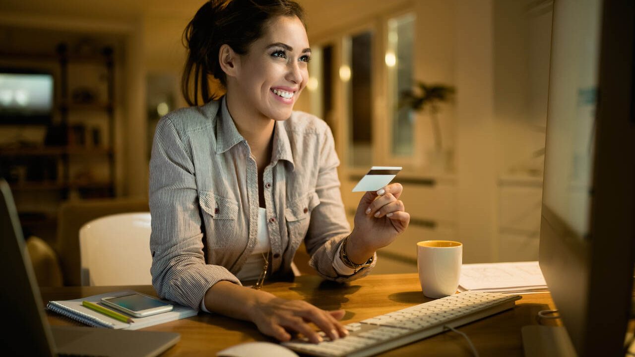 Jovem sorridente pagando contas online com o cartão