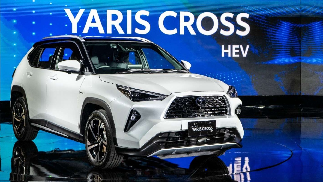 Visual externo do novo Toyota Yaris Cross, na cor branca, com detalhes pretos, à frente de telão azul 