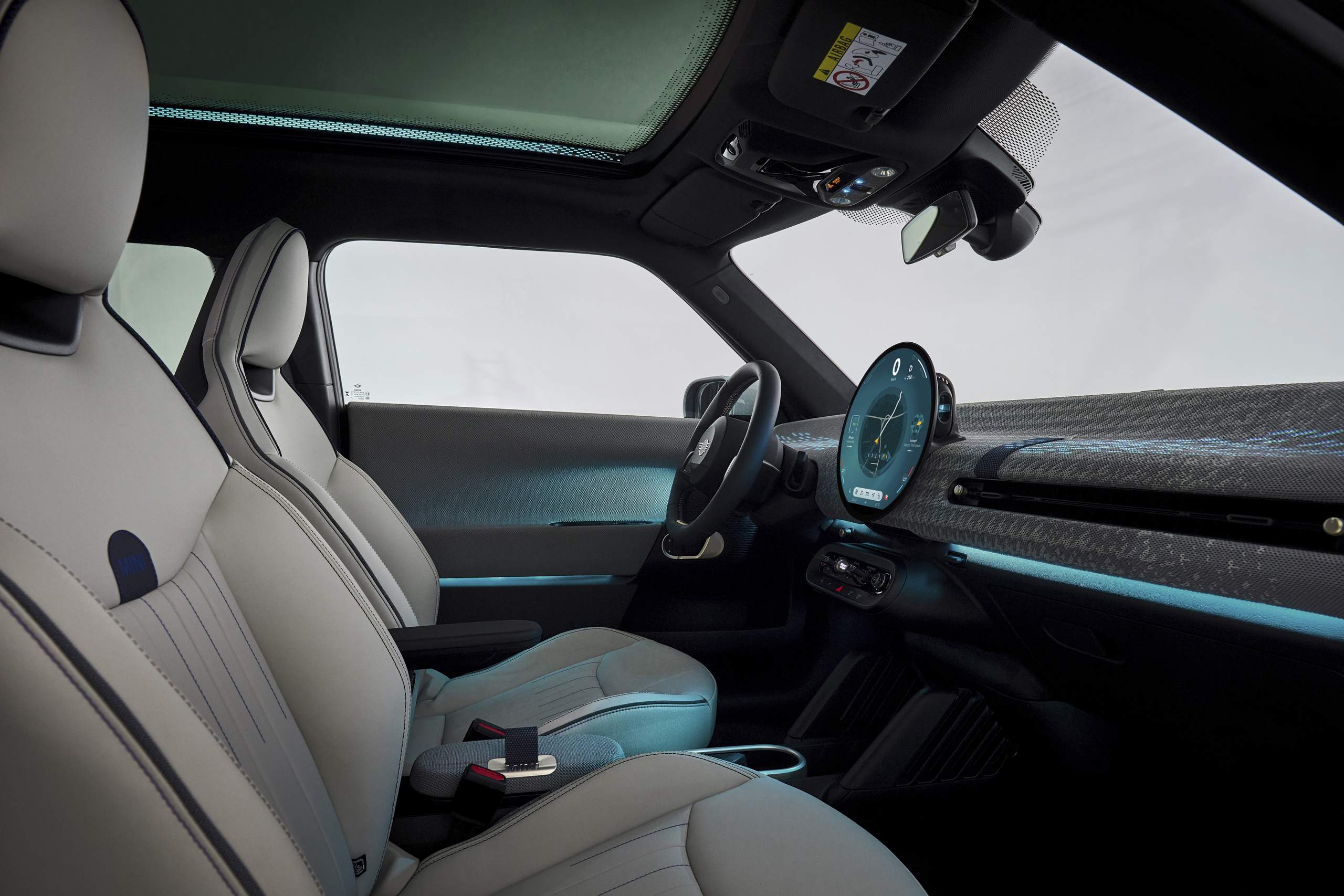 Foto lateral do interior do Mini Cooper SE 2024 , destacando parte dos bancos, painel e volante
