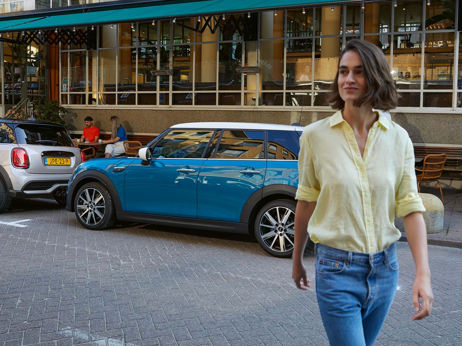 Mulher caminhando à frente do MINI Cooper S 2024, estacionado em frente a um restaurante