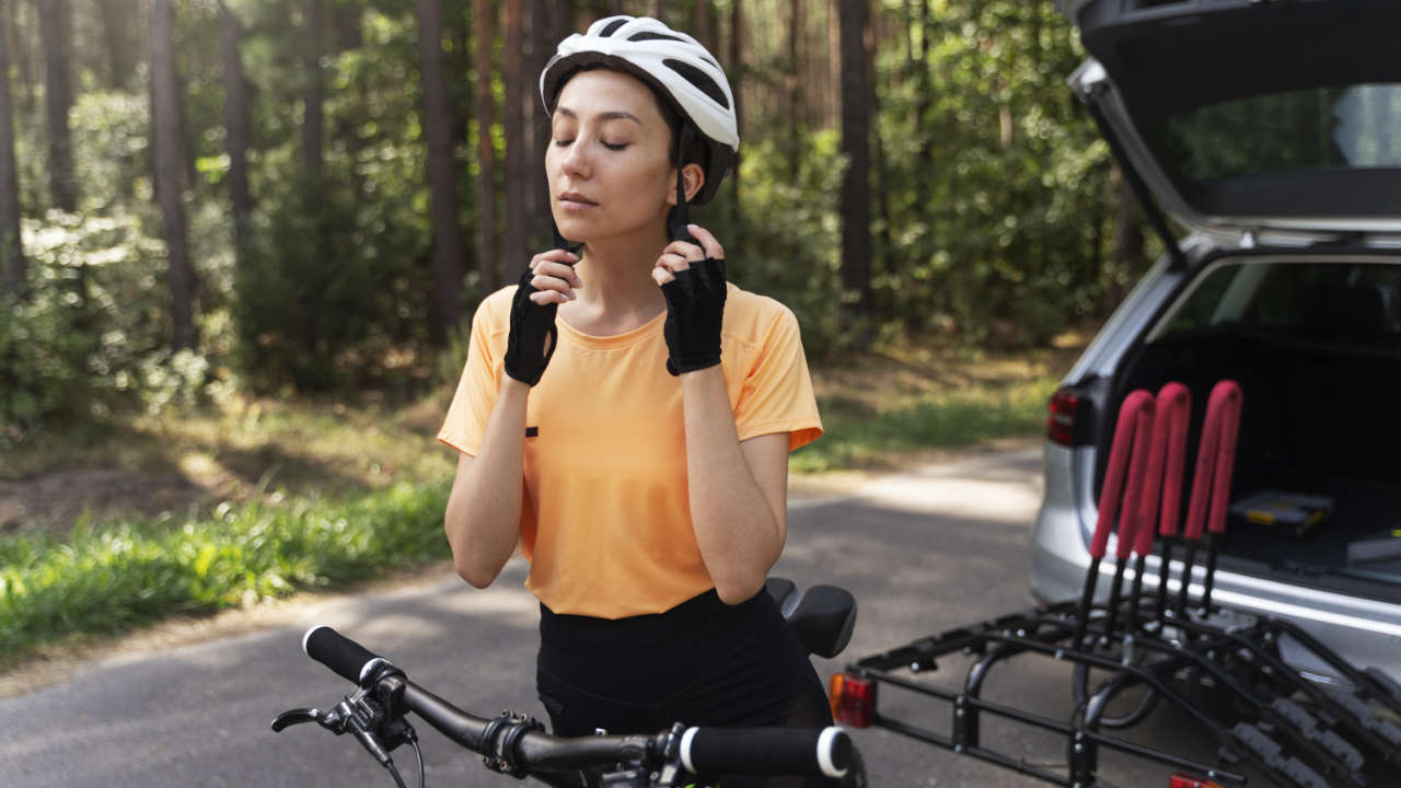 Mulher colocando capacete enquanto monta em bicicleta que acabou de tirar do carro